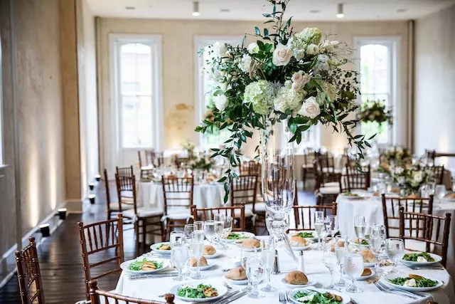 a table set for a formal dinner with white flowers and greenery